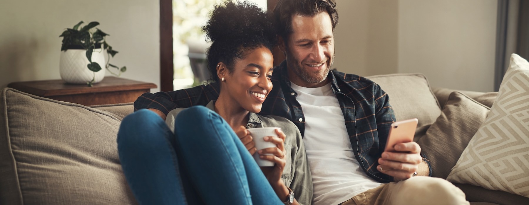 a man and woman sitting on a couch and looking at a cell phone