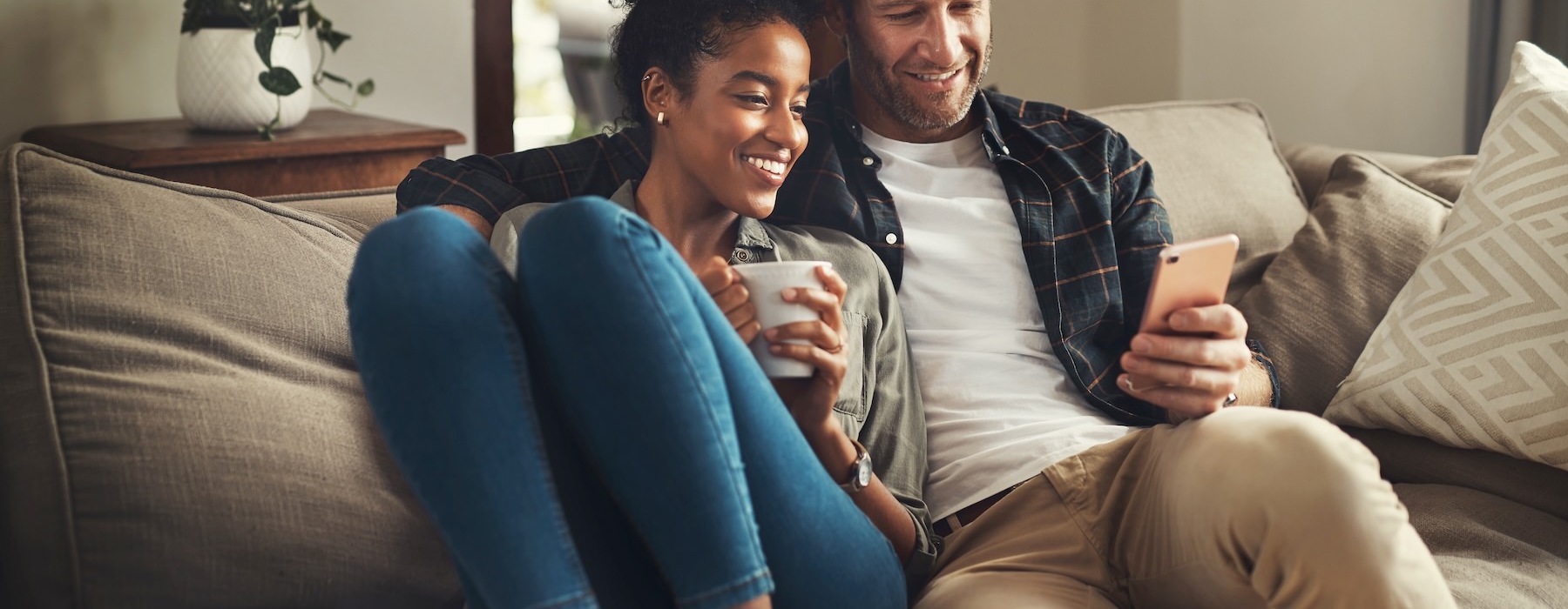 a man and woman sitting on a couch and looking at a cell phone